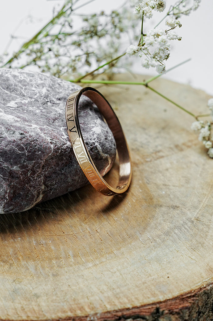 Side view of rose gold Roman style close bangle on a wooden slice
