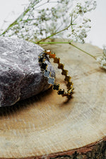 Gold close bangle with black clover design standing on a wooden slice