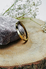 Gold-tone solitaire bangle standing on a wood slice, side view