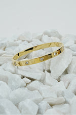 Gold-tone solitaire bangle for women displayed on white stones
