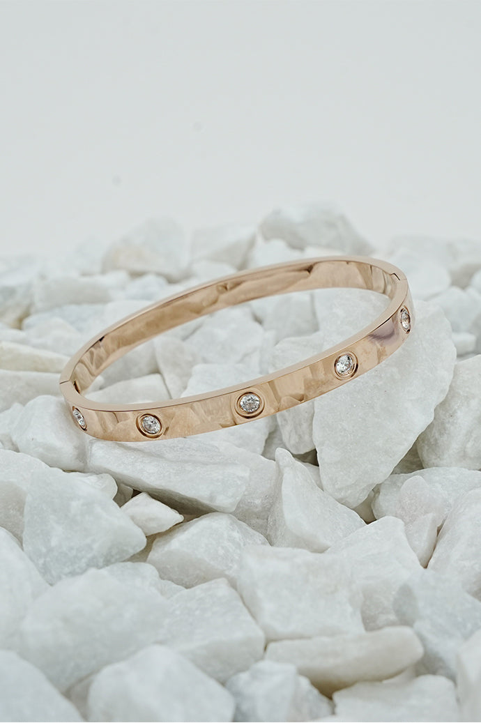 Rose gold-tone solitaire bangle for women displayed on white stones